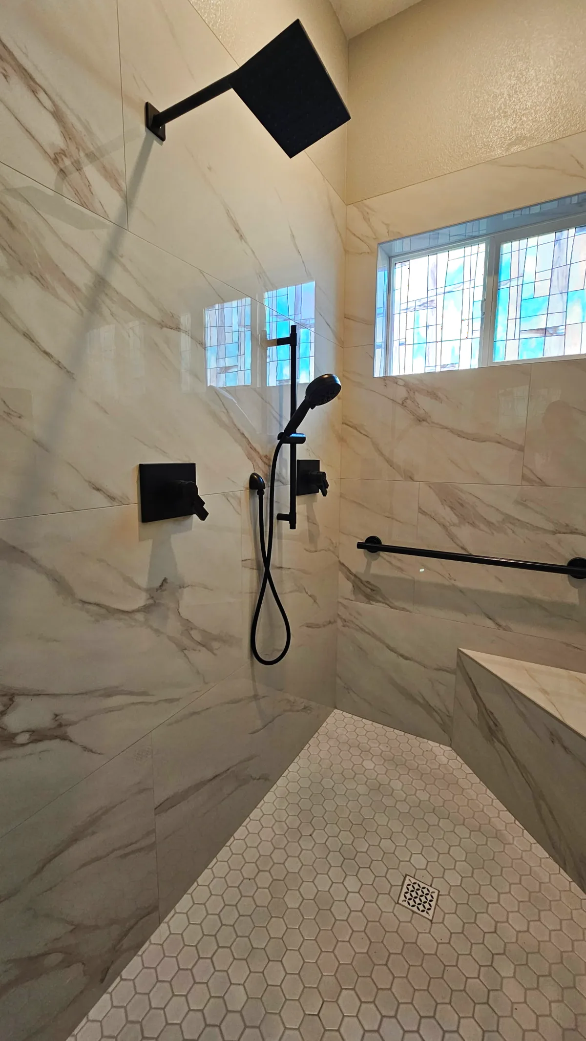 ADA roll-in shower matte black fixture set — square rain head, handheld on vertical slide bar, matte black control, Calacatta porcelain walls, white hex floor